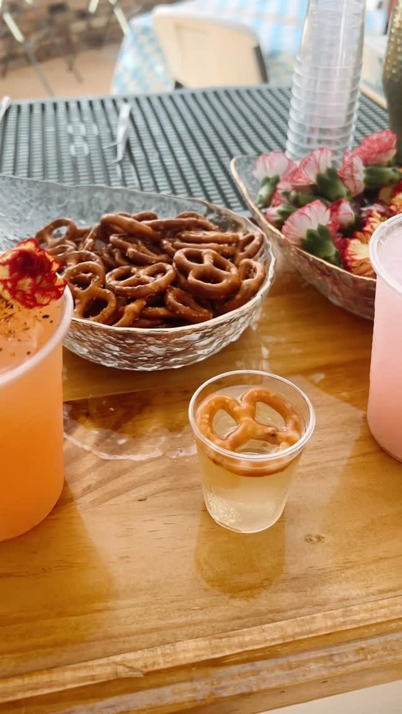 A wooden table with bowls of pretzels, strawberries, and various drinks.