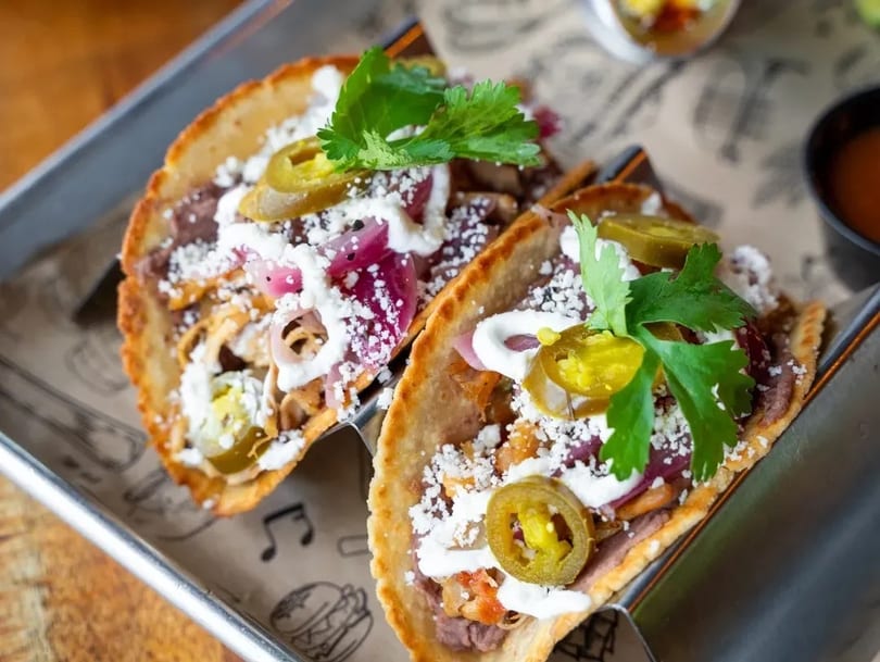 Two crispy tacos filled with meat, beans, cheese, pickled onions, jalapeños, and cilantro.