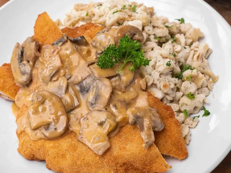 Golden-brown schnitzel topped with creamy mushroom sauce and a side of spaetzle.