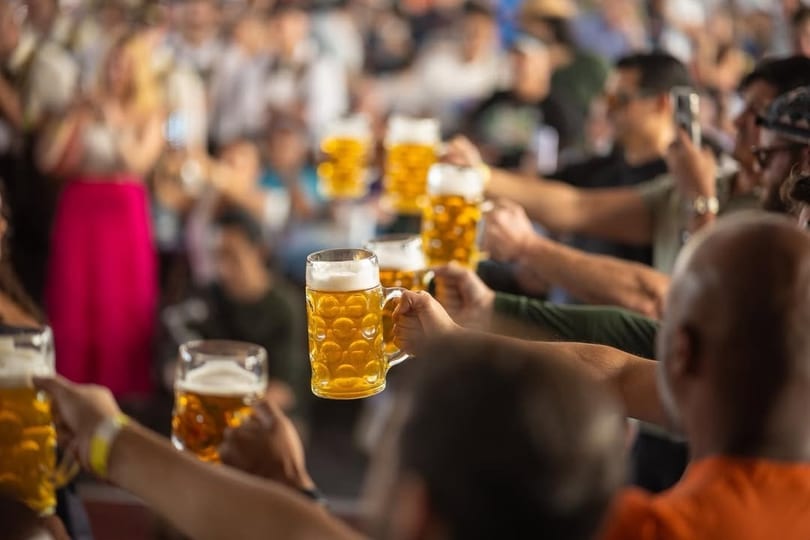 People holding up beer steins in a crowded, festive atmosphere.