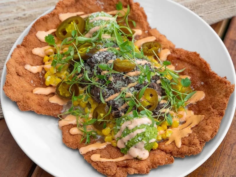 Crispy fried chicken schnitzel topped with black beans, corn, jalapeños, guacamole, and sauce.