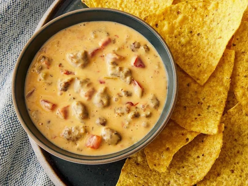 A bowl of creamy queso dip with ground meat and diced tomatoes, served with tortilla chips.